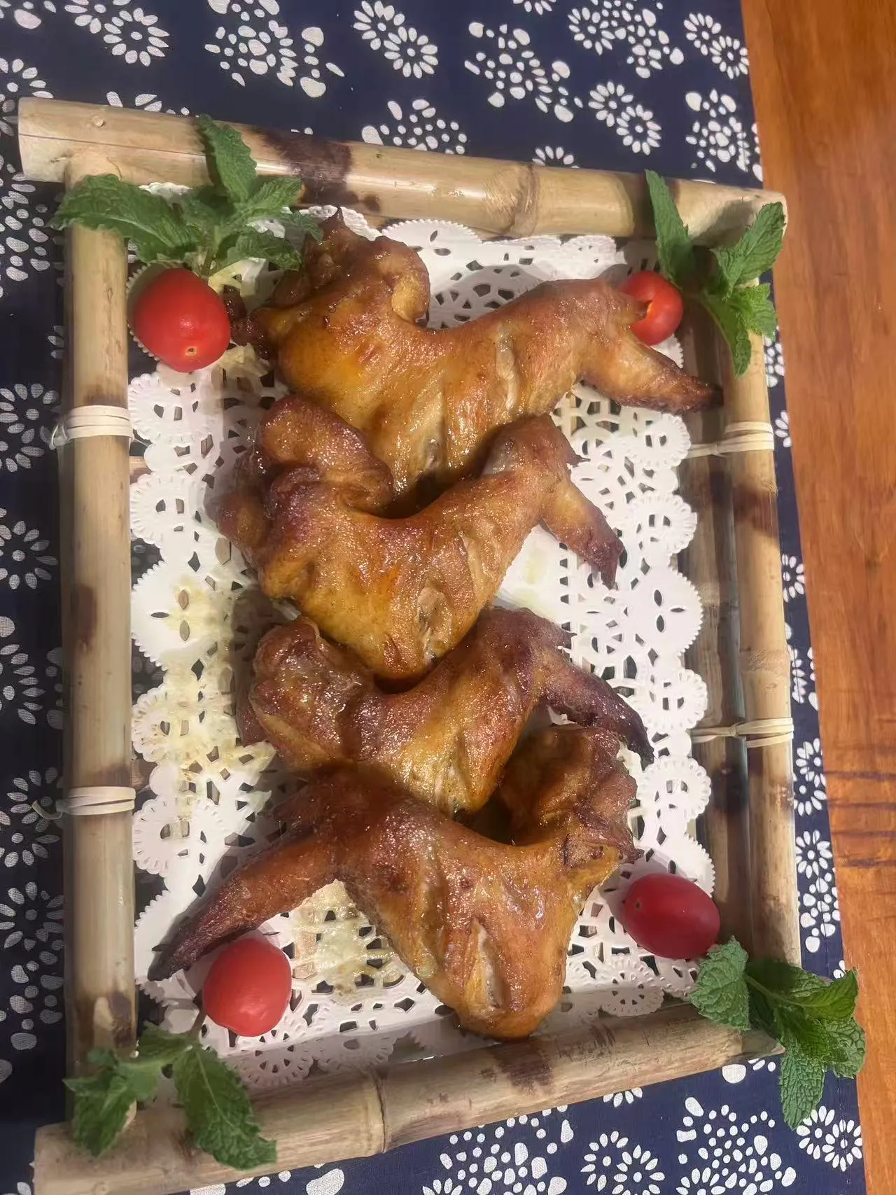 Roasted chicken wings served on bamboo tray with cherry tomatoes and mint sprigs on lace paper liner at Endless Art And Food, an Asian Fushion Restaurant in Catskill