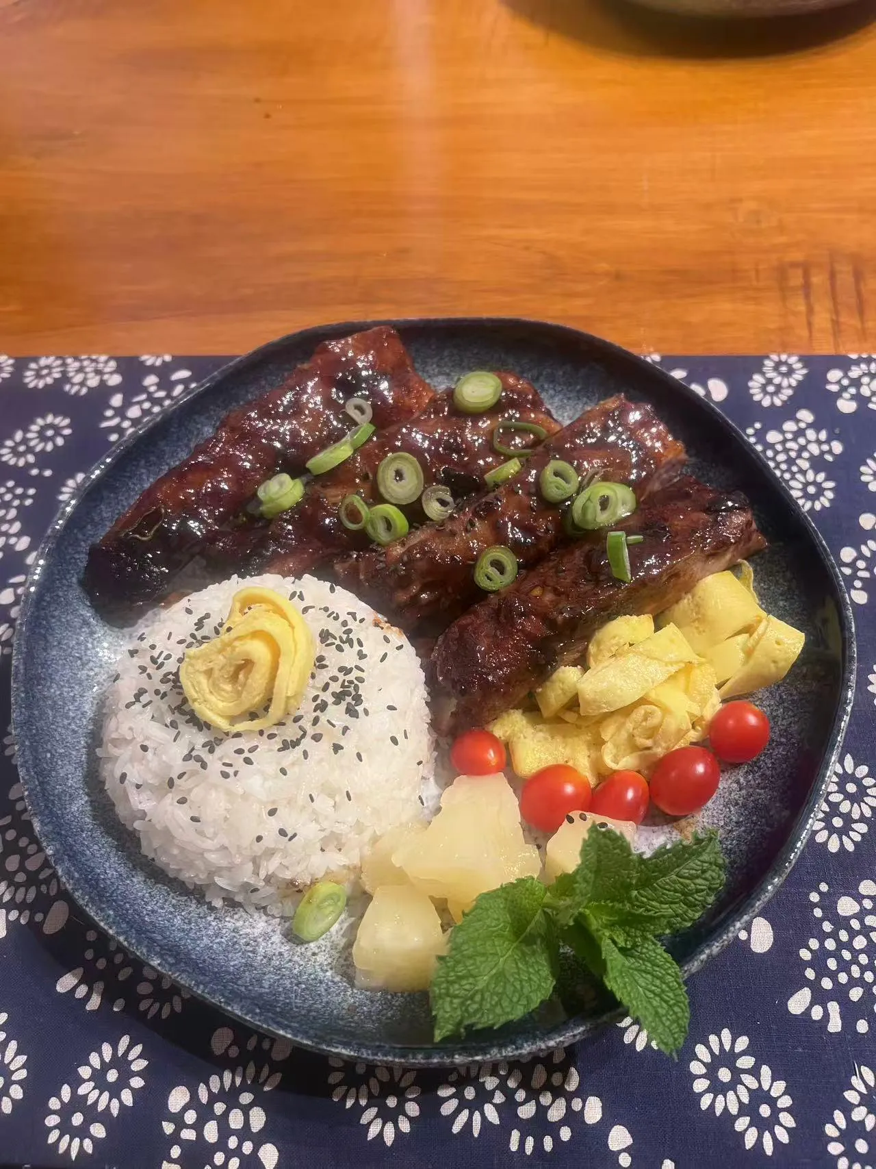 BBQ pork ribs rice bowl with steamed rice, egg roll, pineapple and cherry tomatoes on blue floral cloth at Endless Art And Food, an Asian Fushion Restaurant in Catskill