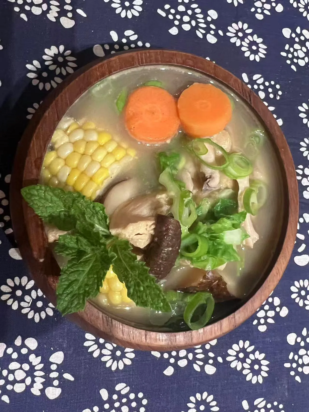 Hearty chicken vegetable soup with corn, carrots, mushrooms and greens in wooden bowl on blue floral cloth at Endless Art And Food, an Asian Fushion Restaurant in Catskill